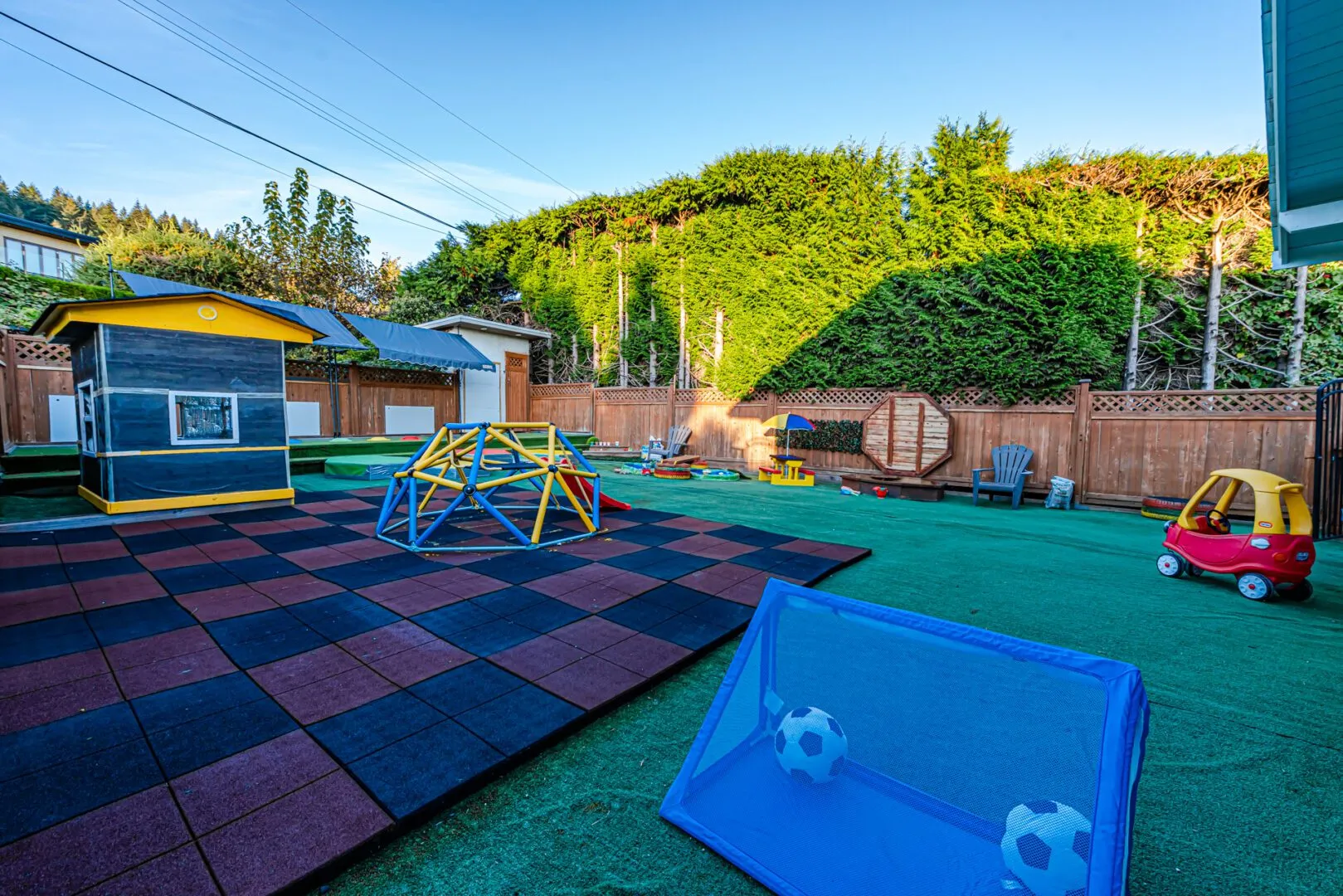 Spacious backyard with a climbing dome, soft play tiles, playhouse and soccer net