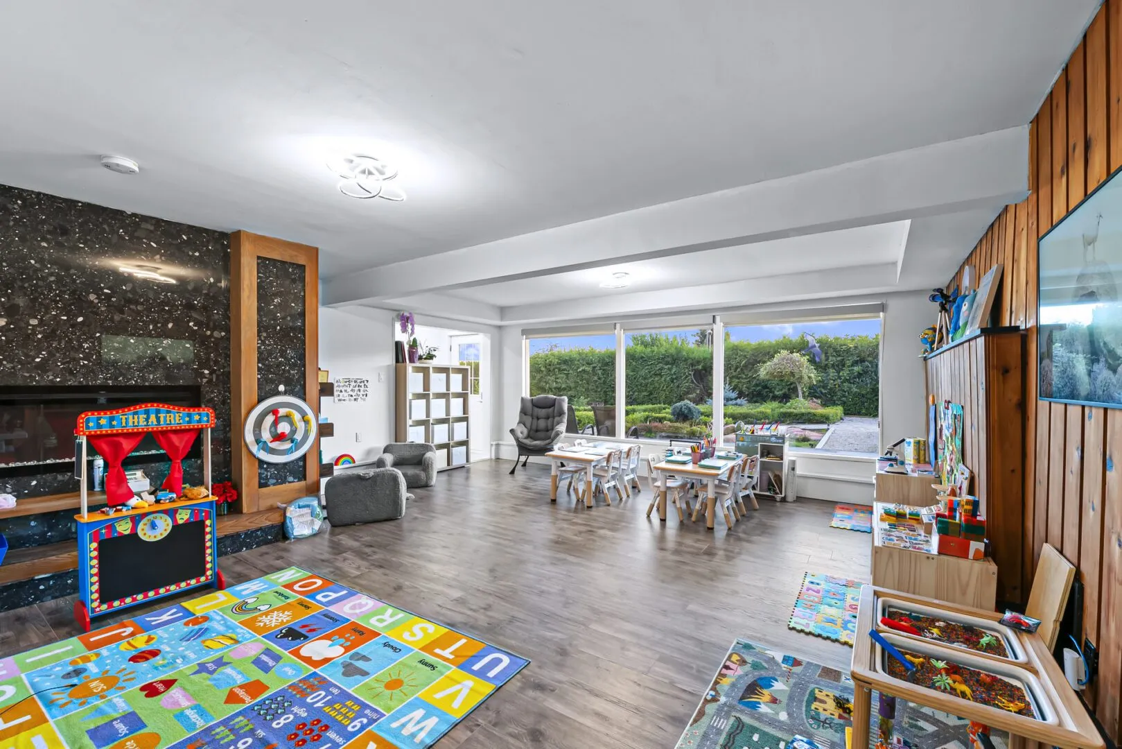 Bright classroom with large windows, alphabet rug, play kitchen and child-sized tables