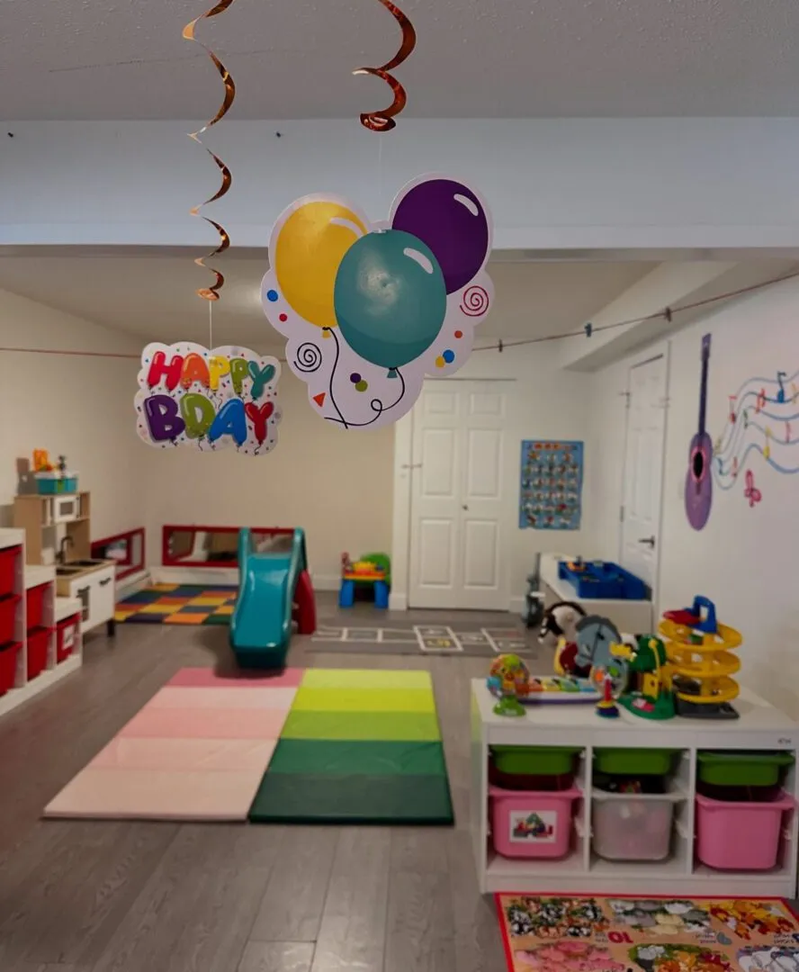 Indoor playroom decorated with birthday balloons, a slide, play mats and toy shelves