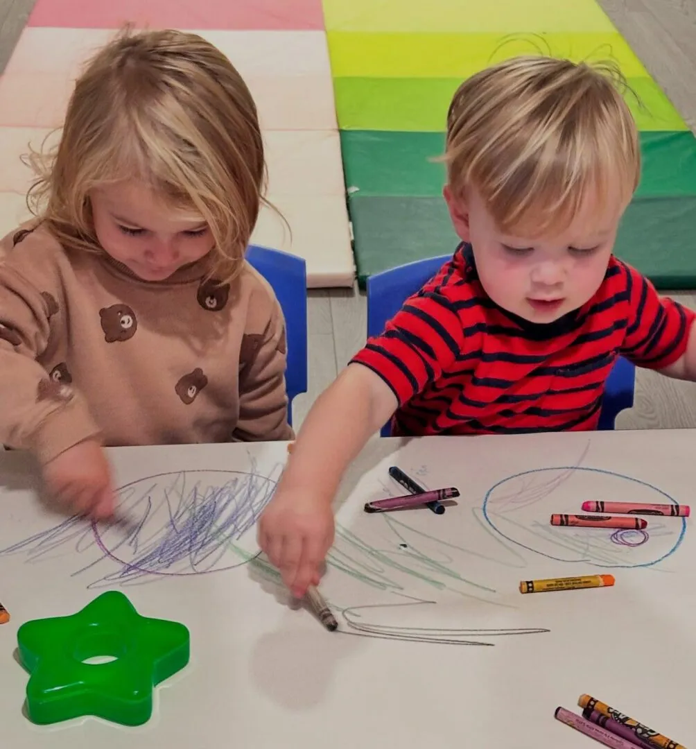 Two toddlers drawing with crayons at a table